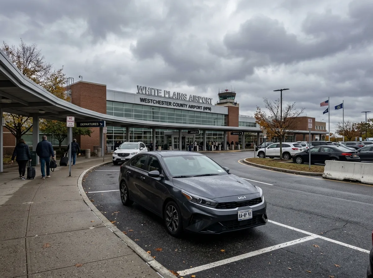 Kia K4 intermediate sedan in dark gray, parked outside White Plains NY terminal, overcast sky